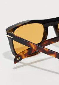Schildpatt Sonnenbrille mit gelb getönten Gläsern, die ein massives Design, schlanke Bügel mit metallischen Akzenten und gekreuzte Arme aufweist.