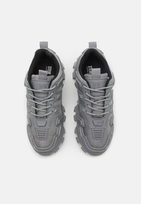 Gray athletic shoes featuring a textured mesh upper, reinforced toe cap, and thick, treaded rubber sole. Includes lace-up closure and pull tab.