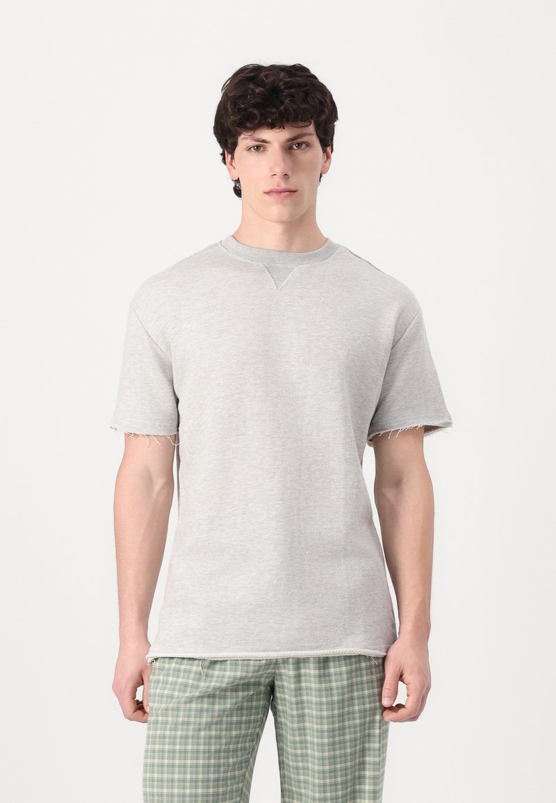 Tricou gri cu mâneci scurte, cu tiv brut și gât rotund, fabricat dintr-un material moale. Purtați cu pantaloni verzi cu carouri.