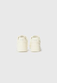 Cream-colored sneakers with a simple design, featuring the brand name "JACK & JONES" embossed on the heel. Set against a plain background.