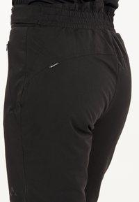 Mustat urheiluleggingsit, joissa on joustava vyötärö, sileä pinta, sivuesiluk pockets, ja pieni logo-yksityiskohta takana.