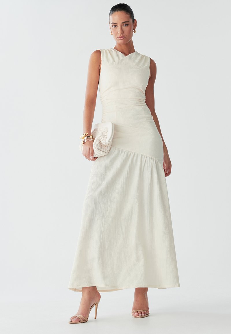 Vestido maxi blanco con textura acanalada, corpiño ajustado y falda acampanada. Combinado con un bolso de mano texturizado y sandalias de tacón alto.