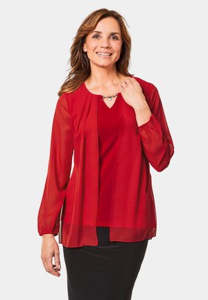 Rode blouse met doorzichtige lange mouwen, een keyhole halslijn en een decoratieve hardware-detail bij de kraag. Gladde textuur en losse pasvorm.