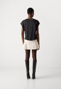 Schwarzes kurzärmliges Oberteil mit einem strukturierten Glanz, kombiniert mit einem cremefarbenen plissierten Minirock und schulterhohen schwarzen Stiefeletten mit Absatz.