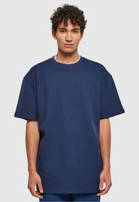 Tengerészkék, oversized póló struktúrált anyagból, kerek nyakkal és rövid ujjakkal. Egyenes szegély minimalista dizájn részletekkel.