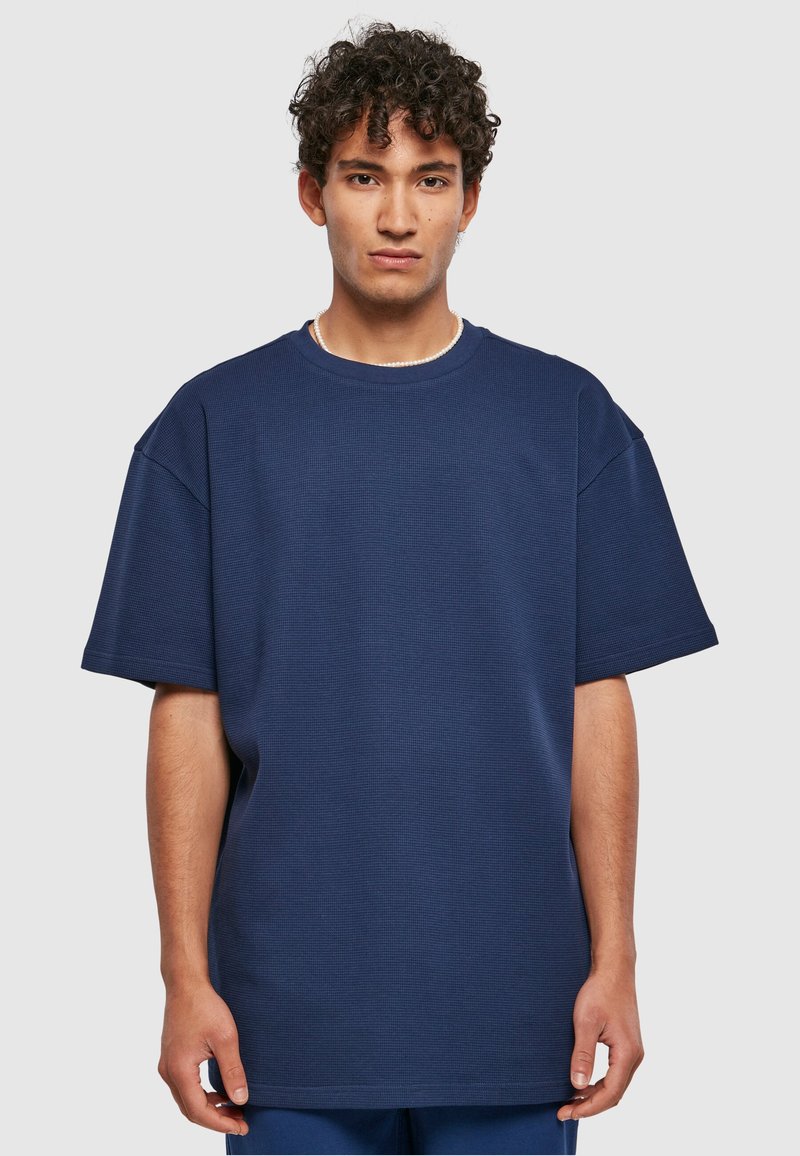 Tengerészkék, oversized póló struktúrált anyagból, kerek nyakkal és rövid ujjakkal. Egyenes szegély minimalista dizájn részletekkel.