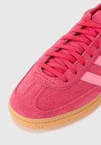 Lyserøde ruskinds sneakers med matchende snørebånd og gummisål. Har kontrasterende lyserøde striber på siderne og teksturerede stikninger som detaljer.