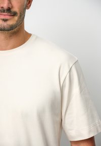 Beżowa bawełniana koszulka z okrągłym dekoltem i krótkimi rękawami, charakteryzująca się gładką fakturą i minimalistycznym wzornictwem.