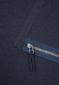 Maglione lavorato a maglia blu navy con tasca con zip e bordo in tessuto blu e zip argentata, superficie testurizzata e vestibilità rilassata.