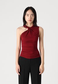 Top sin mangas color marrón, con un detalle en el cuello retorcido, tejido elástico y diseño fruncido, combinado con pantalones negros de cintura alta.