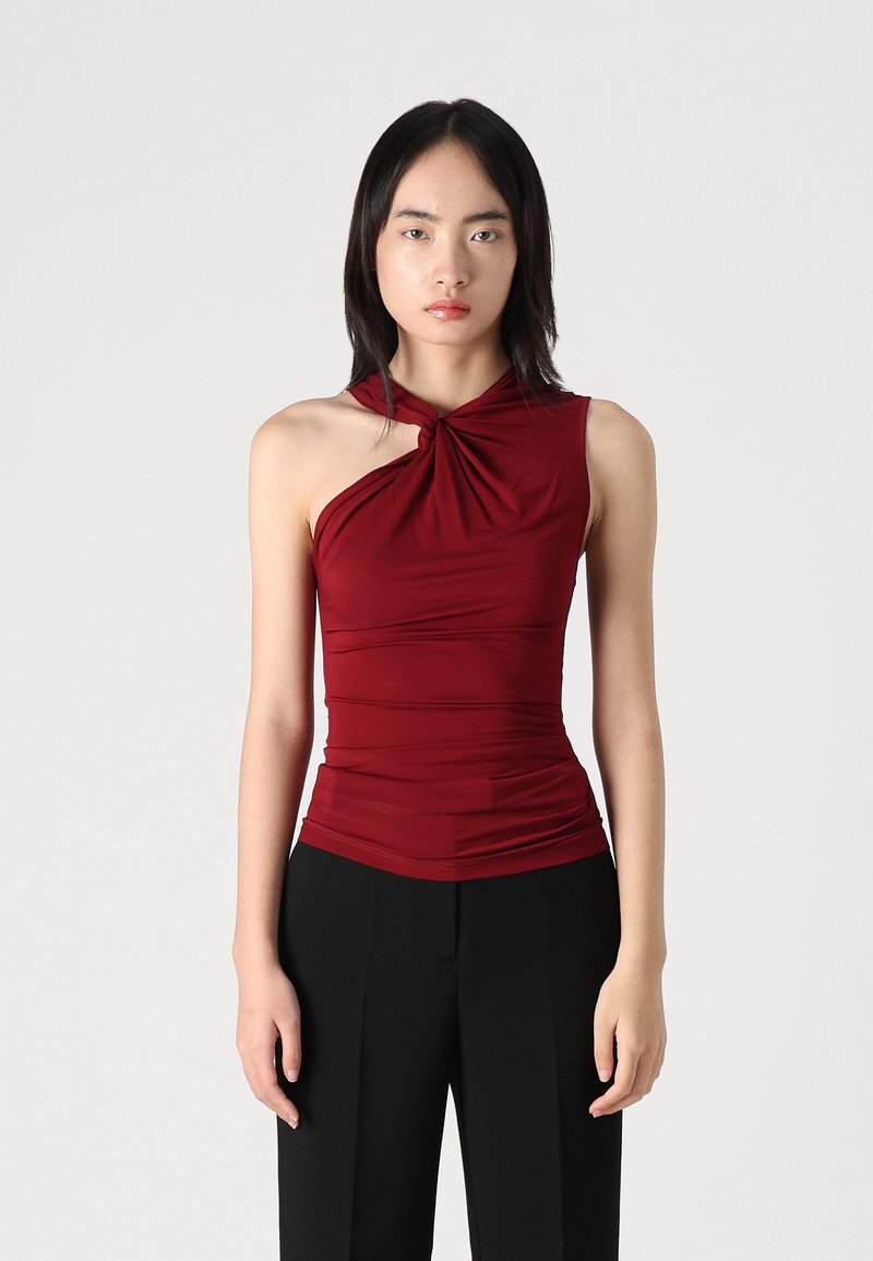 Top sin mangas color marrón, con un detalle en el cuello retorcido, tejido elástico y diseño fruncido, combinado con pantalones negros de cintura alta.