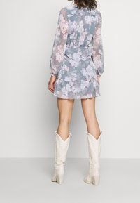 Ljusblå mini-klänning med blommönster i genomskinligt material, med långa ärmar och volangkant, kombinerad med vita knästövlar.