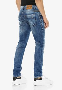 Blauwe denim jeans met een slim fit, zichtbare vervaging en whiskering-details. Heeft twee achterzakken en branding op de tailleband.