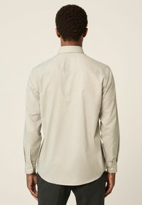 Helles graues Langarmshirt mit Kragen zum Knöpfen, glatter Textur und sichtbaren Knöpfen an den Manschetten, von hinten betrachtet.