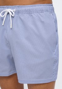 Κοντινό πλάνο ενός ατόμου που φορά μπλε και άσπρα ριγωτά μαγιό με λευκό κορδόνι δεμένο στη μέση.