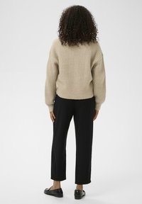 Beige ribbed sweater with dropped shoulders, paired with black straight-leg trousers and glossy black loafers, viewed from behind.