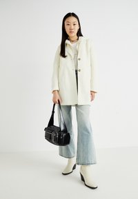 Cappotto bianco in lana con due bottoni, abbinato a jeans svasati in denim chiaro. Borsa a spalla nera e stivaletti chiari con tacco triangolare.
