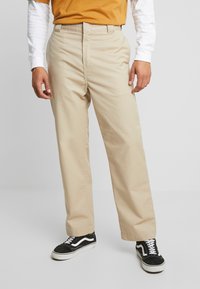 Beige puuvillachino-housut suoralinjaisella designilla, vyölenkeillä ja sivutaskuilla. Yhdistetty mustavalkoisiin lenkkareihin kontrastiksi.