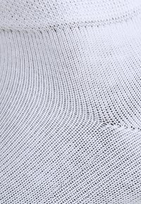 Tissu en mesh blanc avec un tissage doux et ouvert, présentant une légère texture et un motif uniforme, créant une apparence fluide et flexible.