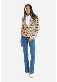 Multicolored blazer featuring a pattern of circles, with a fitted design. Paired with light blue flared jeans and white sneakers.