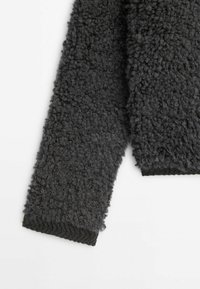 Manche de veste en polaire gris foncé texturée avec poignet côtelé sur fond blanc.