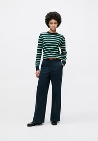 Πλεκτό πουλόβερ με ριγέ πράσινες και ναυτικές ταινίες, συνδυασμένο με σκούρο μπλε παντελόνι φαρδιάς γραμμής, ολοκληρωμένο με καφέ ζώνη και μαύρα παπούτσια.