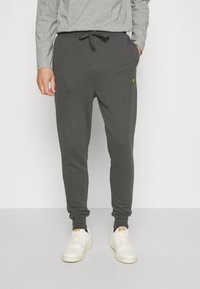 Grijze sweatpants met elastische boorden en een elastische tailleband. Voorzien van een trekkoord en een klein geel logo aan de voorkant. Gemaakt van zacht, gestructureerd materiaal.
