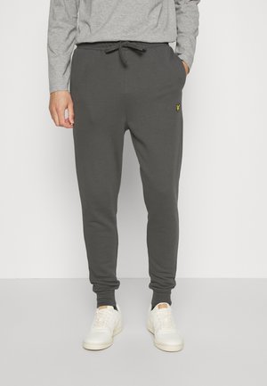 Grå sweatpants med elastiska muddar och midjeband. Har en dragsko och en liten gul logotyp på framsidan. Tillverkad av mjukt, strukturerat material.