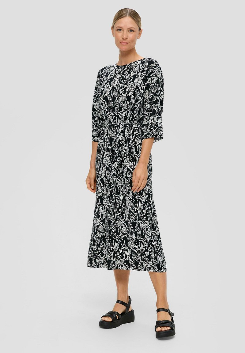 Zwart-wit gemarmerde midi-jurk met driekwart mouwen, een aansluitende taille en een vloeiende rok. Gecombineerd met zwarte platform sandalen.