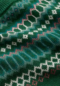 Pleten pulover z zeleno osnovo, ki ima geometrijske vzorce v beli, roza in teal barvi. Mehka tekstura z različno gostoto šivov.