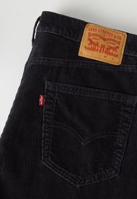 Μαύροι βελούδινοι παντελόνες Levi's που δείχνουν την πίσω τσέπη, την κόκκινη ετικέτα Levi's και την κόκκινη ετικέτα από δέρμα στη μέση.
