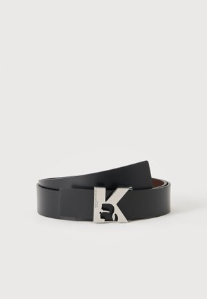 Zwarte leren riem opgerold met een zilverkleurige metalen gesp in de vorm van de letter K met een uitsnede van een gezichtsprofiel.