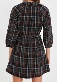 Kárované šaty v námořnické, vínové a krémové barvě. Mají vypasovaný pas, tříčtvrteční rukávy a límec. Vyrobené z texturované látky.