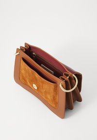 Tan læder håndtaske med en ruskind frontlomme, guldfarvet hardware, lynlåslukning og en dyb rød inderside. Har flere rum.