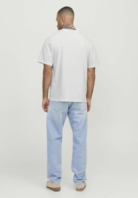 T-shirt bianco in cotone a maniche corte, vestibilità comoda, abbinato a jeans in denim azzurro chiaro. I dettagli notevoli includono una sciarpa a fantasia a contrasto intorno al collo.