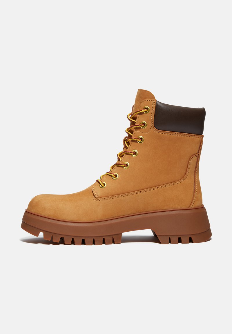 Stivali da trekking in pelle tan con accenti marroni, occhielli dorati e una suola in gomma robusta. Altezza fino al polpaccio con un design con lacci.