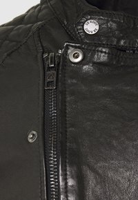 Svart läderjacka med texturerad yta, dragkedja fram, tryckknappsdetaljer och ribbad krage.