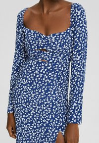 Blue floral dress with long sleeves, featuring a sweetheart neckline and cutouts at the waist. Made of lightweight fabric with a textured pattern.