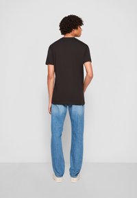 Zwarte T-shirt met korte mouwen en ronde hals, gecombineerd met lichtblauwe denim jeans. Soepele textuur met een relaxte pasvorm en rechte pijpen.