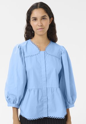 Light blue cotton blouse with puff sleeves, scalloped neckline, and hem detailing. Features a button-front design and a gathered waist.