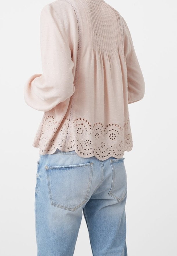 Top a maniche lunghe rosa chiaro con schiena plissettata e orlo scalloppato, caratterizzato da ritagli a occhio. Abbinato a jeans azzurri leggeri.