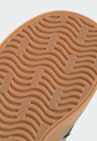 Close-up of a shoe sole with a tan wavy tread pattern and textured oval grips for enhanced traction.