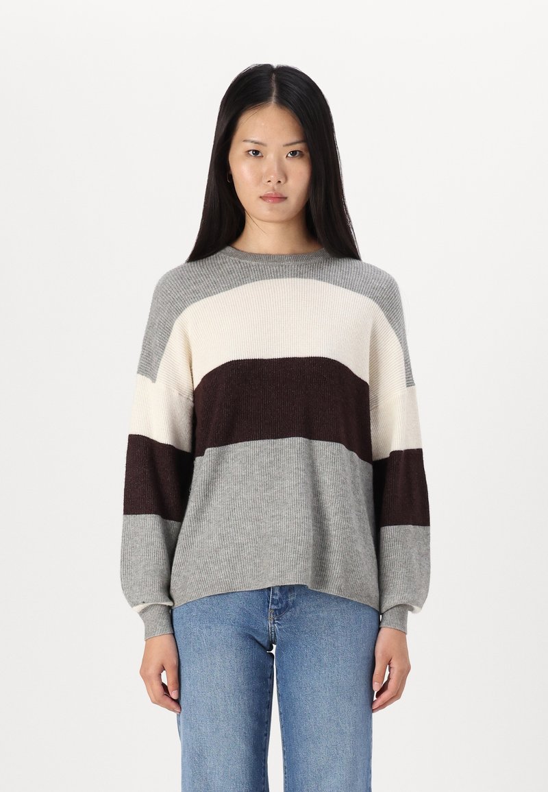 Pull en tricot avec des rayures grises, crème et bordeaux. Encolure ronde, manches longues, texture côtelée et coupe décontractée. Associé à un jean bleu clair.