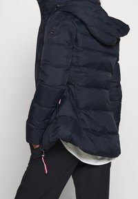 Námořnická pufi bunda s kapucí, s horizontální prošívanou strukturou, logem na rukávu a se zipovou kapsou na hrudi.