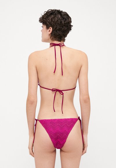 Magenta bikini set features a halter neck with ties and a textured patterned bottom with adjustable side strings, providing a minimalistic design.