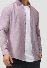 Lys lilla, knap-op skjorte med tekstureret stof, lange ærmer og en brystlomme, lagt over en hvid t-shirt.