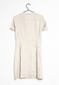 Lněné šaty v jemně béžové barvě, s krátkými rukávy, kulatým výstřihem a skladováním po stranách. Visí na černém háčku.