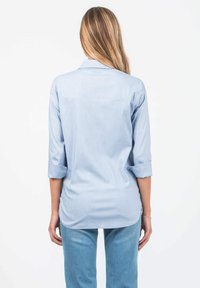 Hellblaues Langarmhemd mit aufgerollten Bündchen, ausgestattet mit einem Rückeneinsatzdesign und glatter Textur, kombiniert mit hellblauen Jeans.