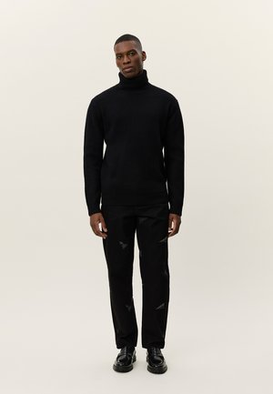 Schwarzer gerippter Rollkragenpullover kombiniert mit schwarzen Hosen, die subtile dreieckige Muster aufweisen, sowie schwarzen Schuhen. Minimalistisches Design, strukturierter Stoff.