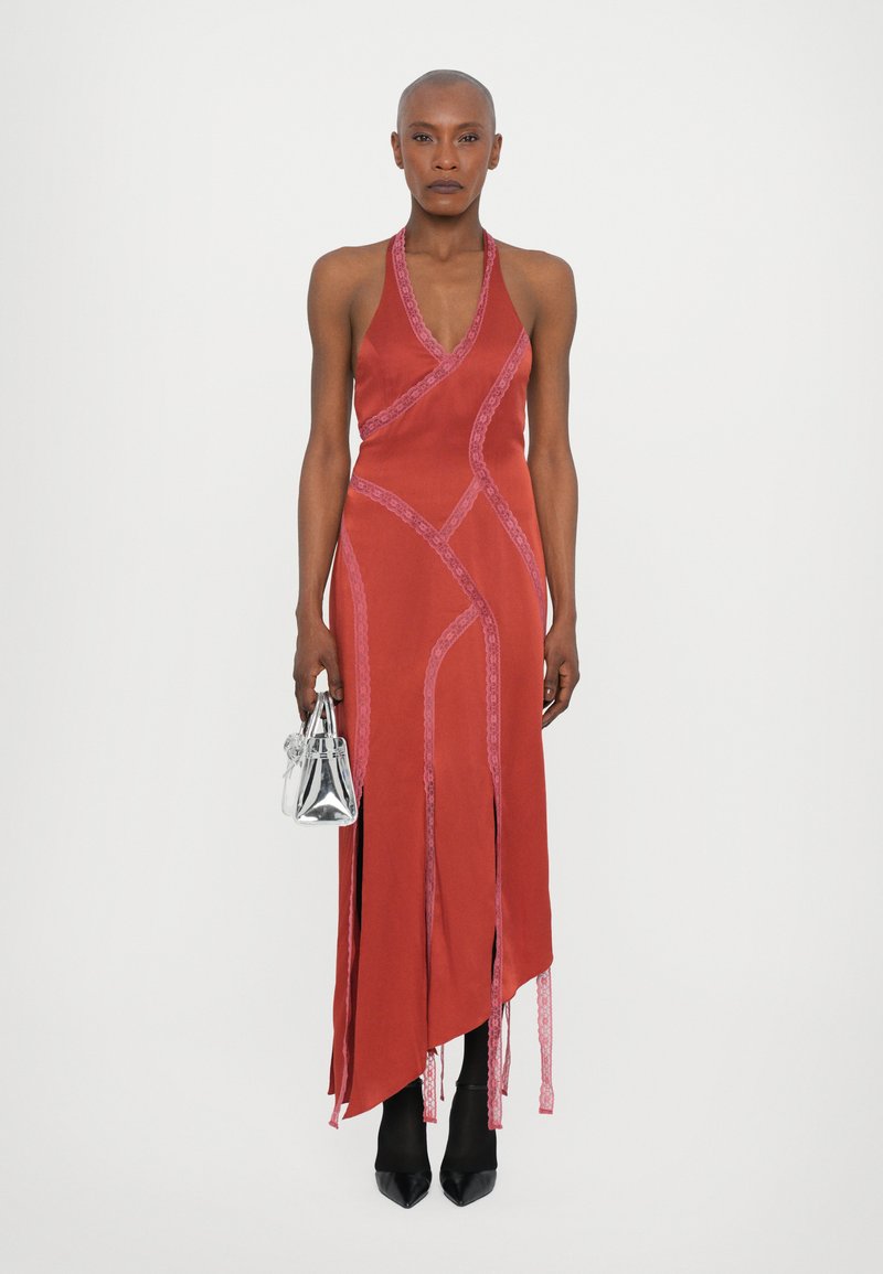 Vestito rosso in satin con dettagli in pizzo, orlo asimmetrico e spacchi laterali. La modella tiene una borsa argentata ed indossa décolleté nere a punta.